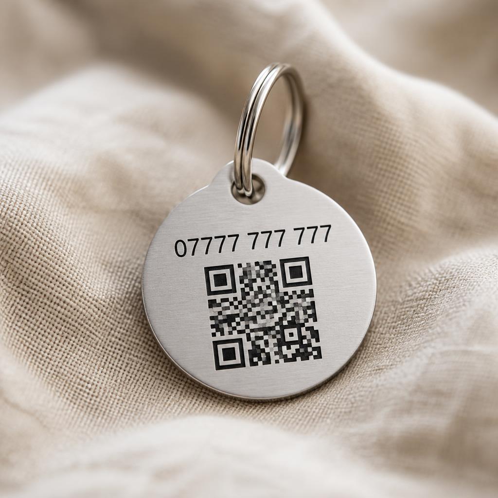 Close-up of a pet ID tag engraved with a mobile number and QR code